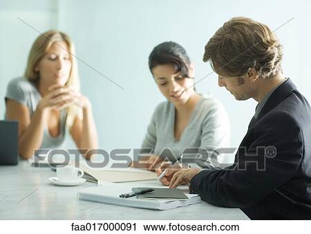 Stock Image - Mature man sitting at table with teenage girl and young female professional, signing document. Fotosearch