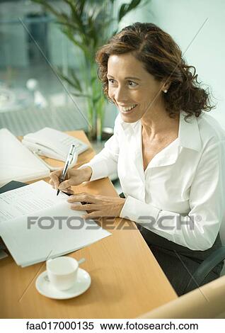Stock Photography - Mature professional woman sitting at table, smiling and looking out of frame. Fotosearch