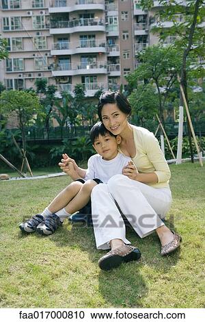 Mother and son sitting on grass in front of apartment building, full length View Large Photo Image Stock Image - Mother and son sitting on grass in front of apartment building, full length. Fotosearch