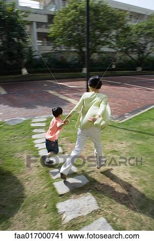 Stock Image - Mother and son walking across grass in apartment complex. Fotosearch