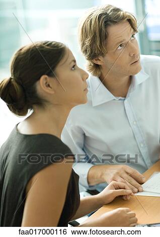 Professional couple sitting at table, looking out of frame View Large Photo Image Stock Photograph - Professional couple sitting at table, looking out of frame. Fotosearch