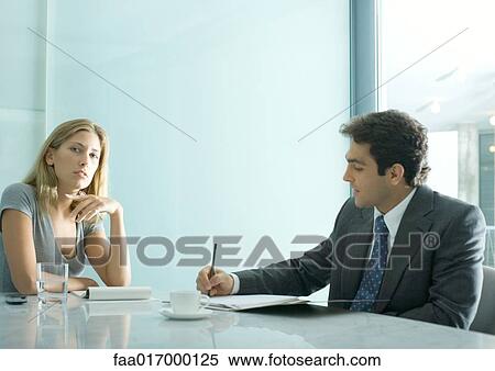 Stock Photography - Professional man and woman having meeting, man taking notes while woman looks at camera. Fotosearch