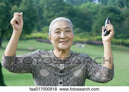 Senior woman raising arms, holding cell phone View Large Photo Image Stock Photo - Senior woman raising arms, holding cell phone. Fotosearch