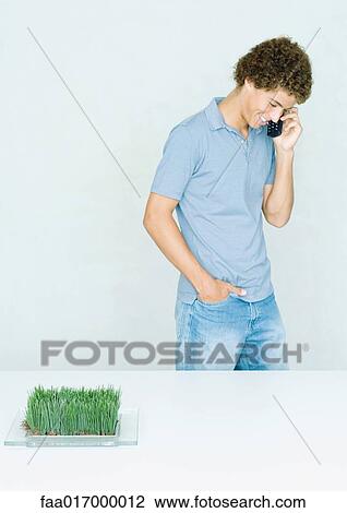 Stock Image - Teenage boy standing, using cell phone. Fotosearch