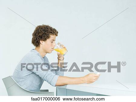Stock Photograph - Teenage boy using cell phone, drinking juice. Fotosearch
