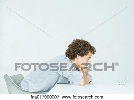 Stock Photo - Teenage boy with head down on arms, looking at cell phone. Fotosearch