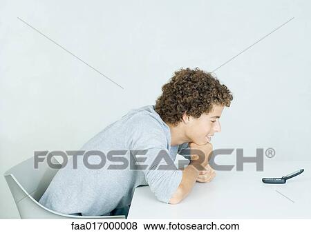 Stock Photo - Teenage boy with head down on arms, looking at cell phone. Fotosearch