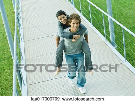 Teenage couple, boy carrying girl piggyback on walkway, smiling at camera View Large Photo Image Stock Photo - Teenage couple, boy carrying girl piggyback on walkway, smiling at camera. Fotosearch