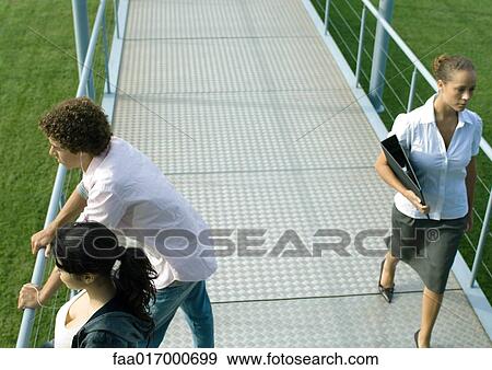 Stock Photo - Teenage couple leaning against rail of walkway while businesswoman walks by. Fotosearch