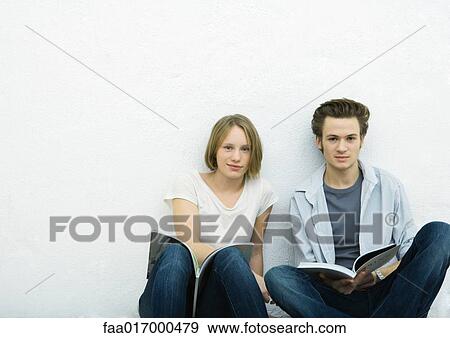 Stock Photo - Teenage girl and young man sitting on floor with books, looking at camera. Fotosearch