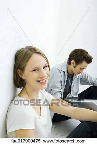 Teenage girl and young man sitting on floor, girl smiling at camera View Large Photo Image Stock Photography - Teenage girl and young man sitting on floor, girl smiling at camera. Fotosearch