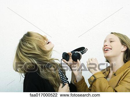 Stock Image - Teenage girl handing friend headphones. Fotosearch