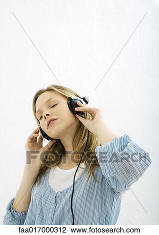 Stock Image - Teenage girl listening to headphones, portrait. Fotosearch