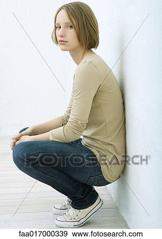 Teenage girl squatting and leaning against wall, looking at camera, portrait View Large Photo Image Stock Photo - Teenage girl squatting and leaning against wall, looking at camera, portrait. Fotosearch