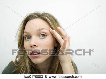 Stock Photo - Teenage girl with finger on temple, leaning toward camera, portrait. Fotosearch