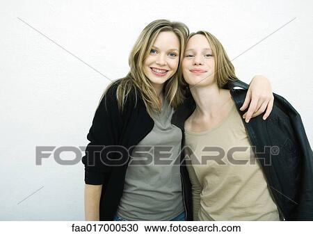 Stock Image - Teenage girls standing side by side, smiling at camera, portrait. Fotosearch