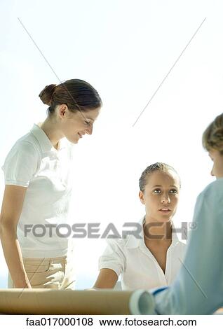 Three adults gathered around blueprints in office View Large Photo Image Stock Photo - Three adults gathered around blueprints in office. Fotosearch