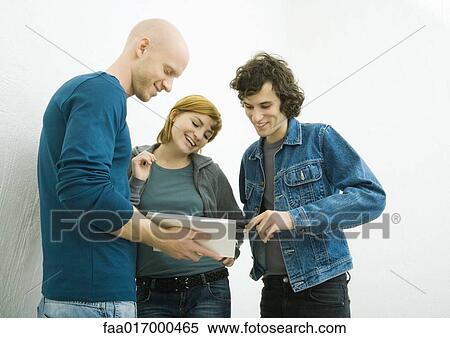 Three young adults looking at book together, smiling View Large Photo Image Stock Photography - Three young adults looking at book together, smiling. Fotosearch