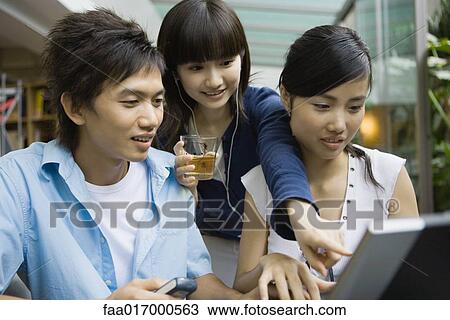 Stock Image - Three young adults using laptop, one pointing at screen. Fotosearch