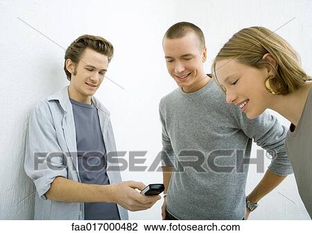 Three young friends looking at cell phone, smiling View Large Photo Image Stock Image - Three young friends looking at cell phone, smiling. Fotosearch
