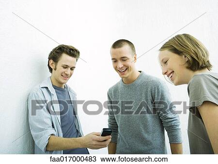 Stock Image - Three young friends looking at cell phone, smiling. Fotosearch