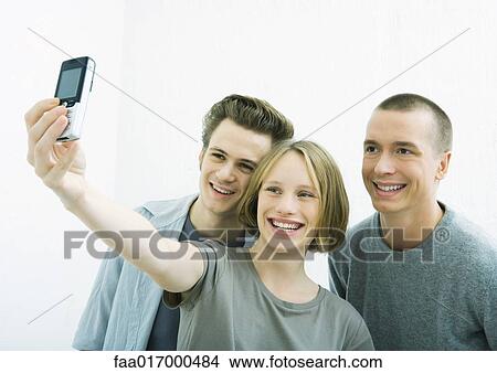 Picture - Three young friends taking photo together with cell phone. Fotosearch