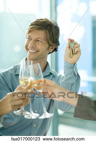 Toasting with glasses of champagne, focus on man holding up keys in background View Large Photo Image Stock Image - Toasting with glasses of champagne, focus on man holding up keys in background. Fotosearch