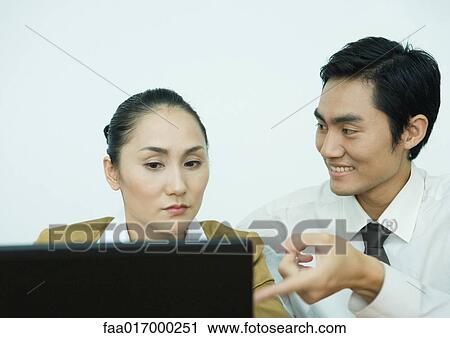 Stock Image - Two business associates using computer, man pointing toward screen. Fotosearch