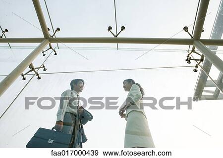 Two business executives standing in glass walkway, talking, low angle view View Large Photo Image Stock Photo - Two business executives standing in glass walkway, talking, low angle view. Fotosearch