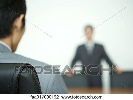 Stock Image - Two businessmen facing each other across conference table, focus on foreground. Fotosearch