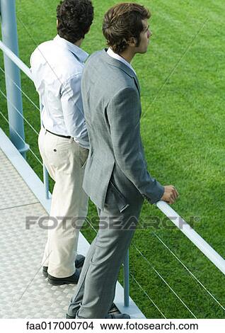Two businessmen standing on walkway looking out of frame View Large Photo Image Picture - Two businessmen standing on walkway looking out of frame. Fotosearch
