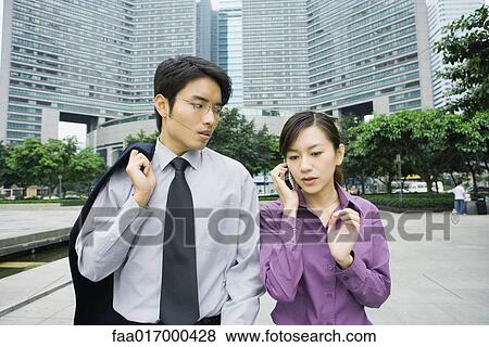Stock Photo - Two executives in business park, woman using cell phone. Fotosearch