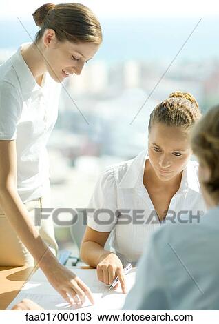 Stock Image - Two women discussing blueprints in office. Fotosearch