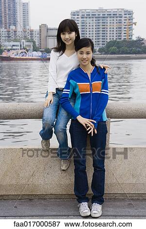 Stock Photo - Two young adult female friends, sitting by river. Fotosearch