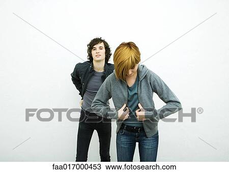 Stock Image - Two young adults putting on jackets, white background. Fotosearch