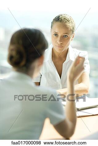 Two young female professionals sitting across from each other, having conversation, focus on woman listening in background View Large Photo Image Stock Photo - Two young female professionals sitting across from each other, having conversation, focus on woman listening in background. Fotosearch