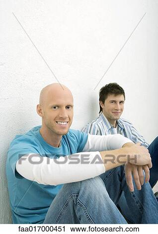 Two young men sitting on floor, looking at camera View Large Photo Image Stock Image - Two young men sitting on floor, looking at camera. Fotosearch