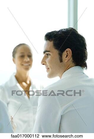 Stock Image - Two young professionals, focus on man in foreground. Fotosearch