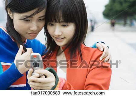 Stock Photo - Two young women friends looking at cell phone together. Fotosearch