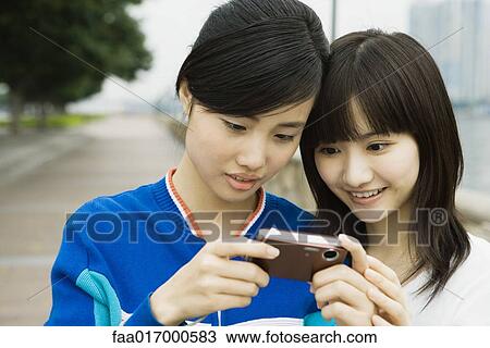 Stock Image - Two young women looking at screen of digital camera together. Fotosearch