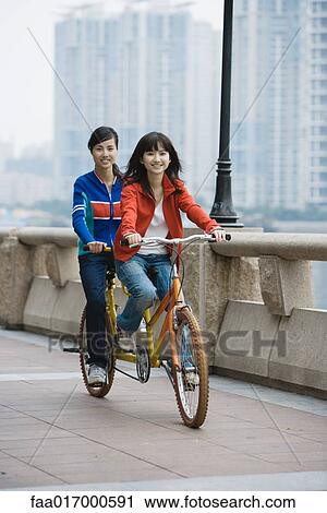 Stock Image - Two young women riding tandem bicycle. Fotosearch