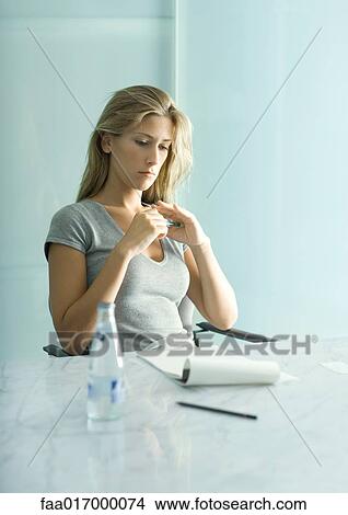 Woman sitting at table with pad of paper, pen and bottle of water, looking down View Large Photo Image Picture - Woman sitting at table with pad of paper, pen and bottle of water, looking down. Fotosearch