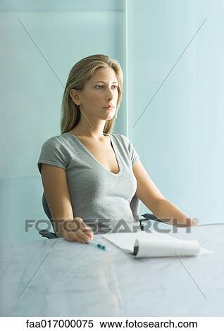 Woman sitting at table with pad of paper, pen and bottle of water, looking down View Large Photo Image Stock Photography - Woman sitting at table with pad of paper, pen and bottle of water, looking down. Fotosearch