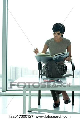 Woman sitting in lobby looking at book View Large Photo Image Stock Photo - Woman sitting in lobby looking at book. Fotosearch