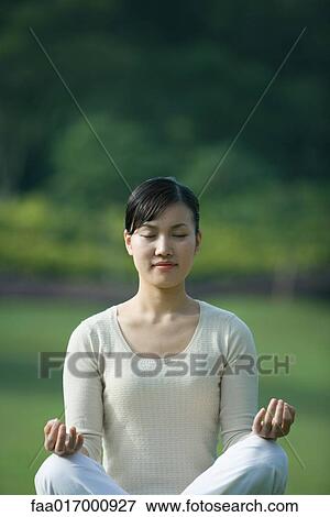 Stock Photo - Woman sitting in lotus position, eyes closed. Fotosearch