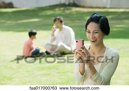 Woman taking photo with digital camera, husband and son in background View Large Photo Image Stock Image - Woman taking photo with digital camera, husband and son in background. Fotosearch