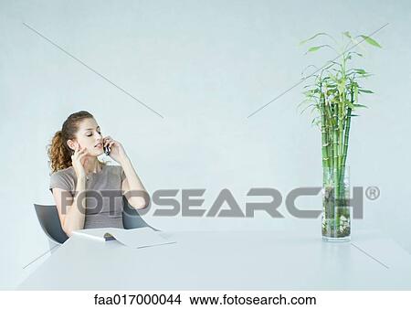 Woman using cell phone, pad of paper on table in front of her View Large Photo Image Picture - Woman using cell phone, pad of paper on table in front of her. Fotosearch