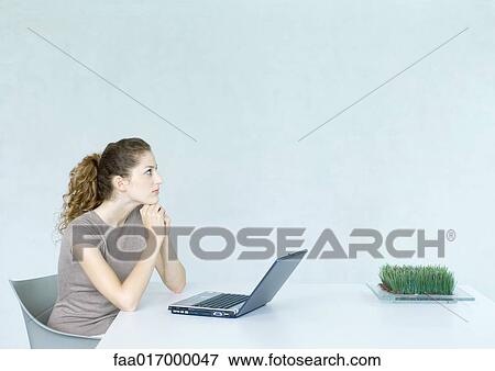 Woman using laptop, looking up, tray of wheatgrass on table View Large Photo Image Stock Photo - Woman using laptop, looking up, tray of wheatgrass on table. Fotosearch