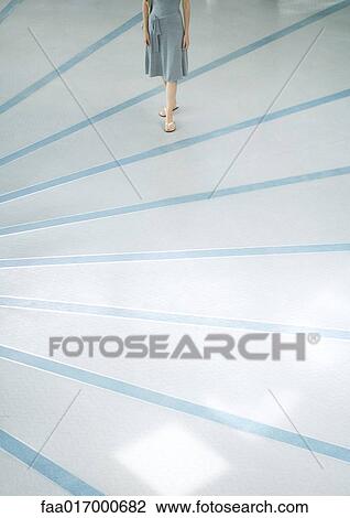 Stock Image - Woman walking across rayed floor, low section. Fotosearch