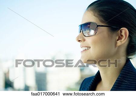 Stock Image - Woman wearing sunglasses, skyline in background, profile. Fotosearch